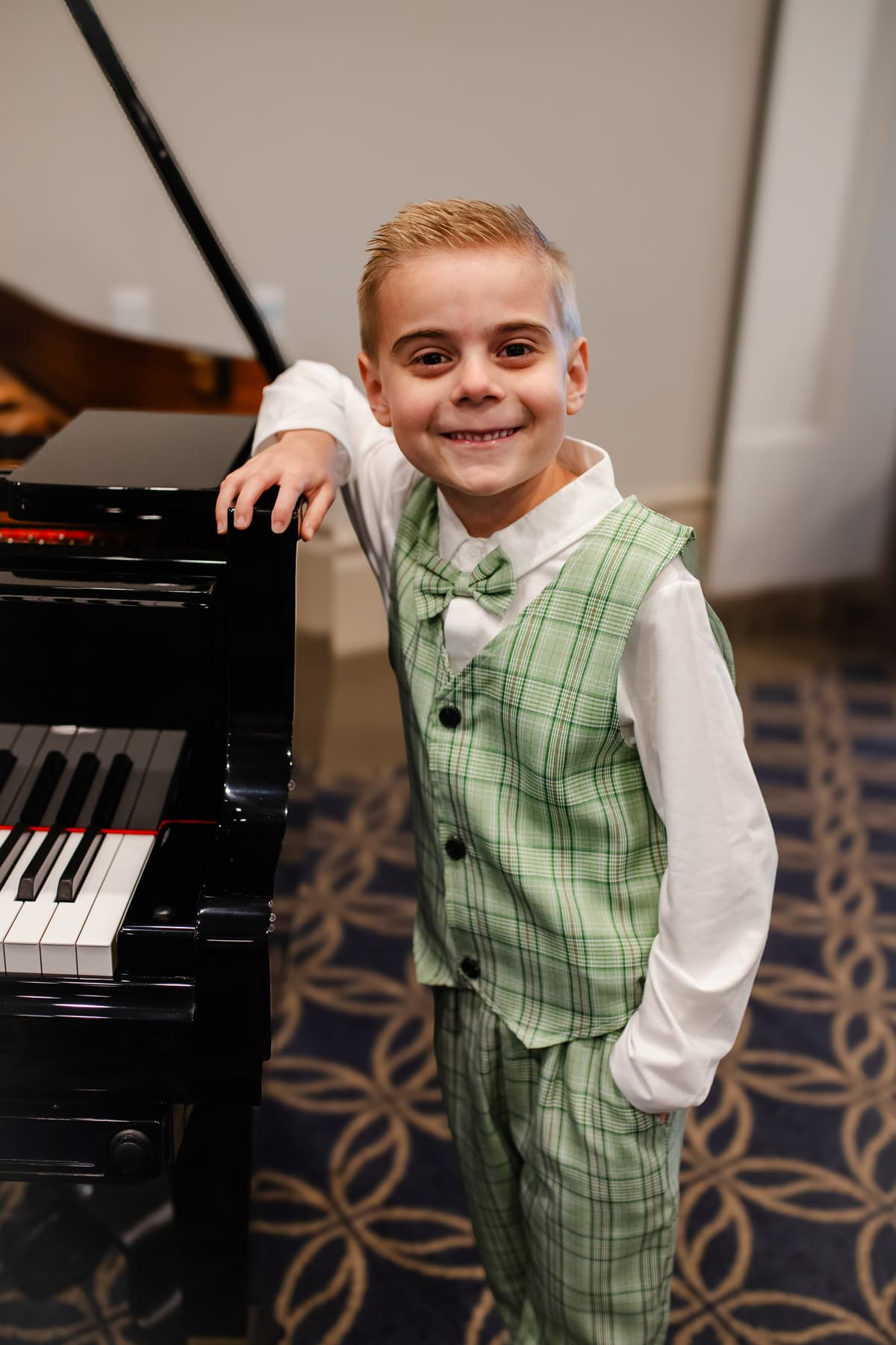 A young student smiling proudly beside the grand piano at the recital